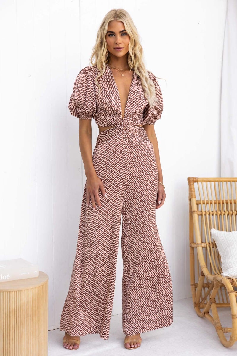 Model wearing Soho Jumpsuit with V-neckline and puff sleeves, featuring a cut-out waist and elegant design.