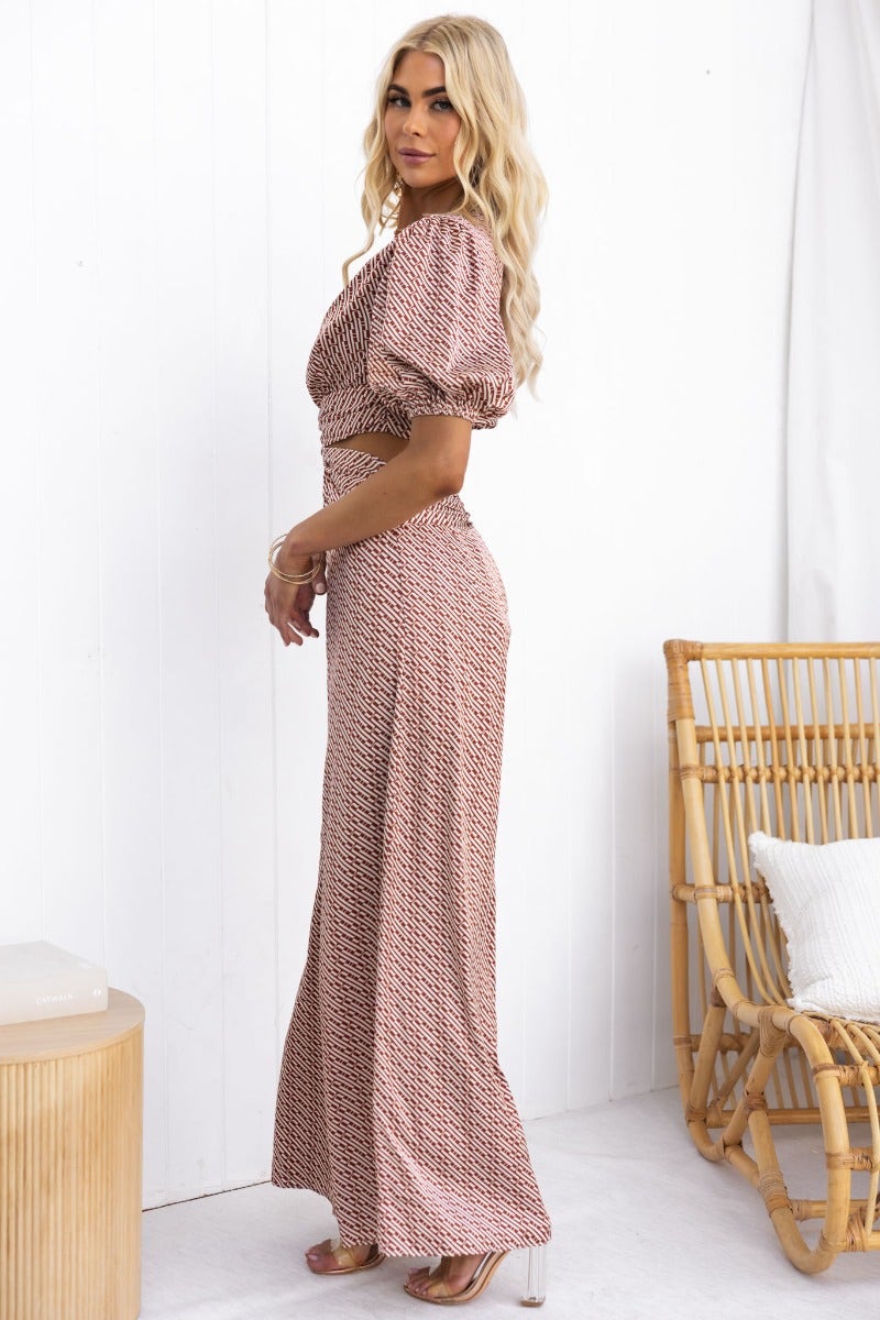 Side view of a woman in a satin Soho jumpsuit with V-neckline and puff sleeves, featuring a cut-out at the waist.