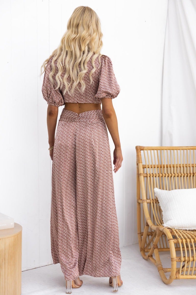 Model wearing a back view of a satin Soho jumpsuit with puff sleeves and cut-out waist detail.