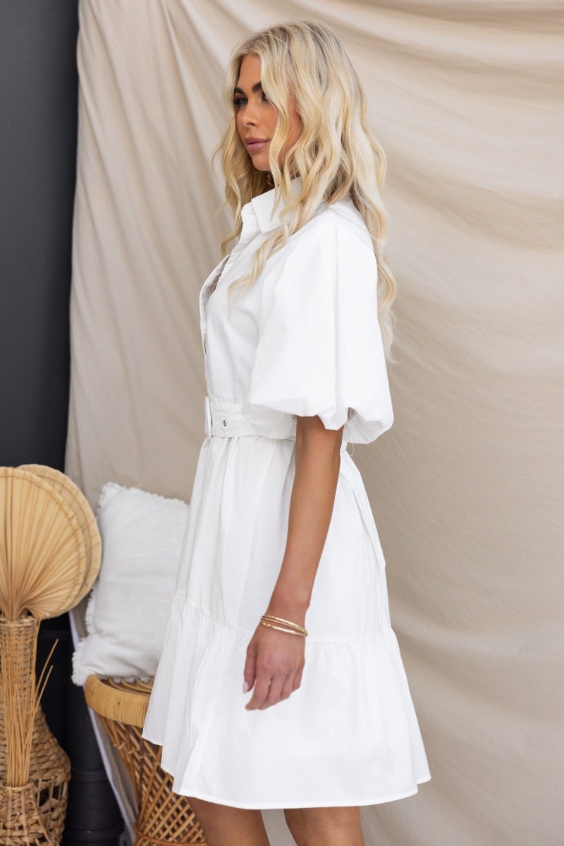 Eloisa Dress: White cotton button-up dress with collar, elastic sleeves, and removable belt, styled casually.