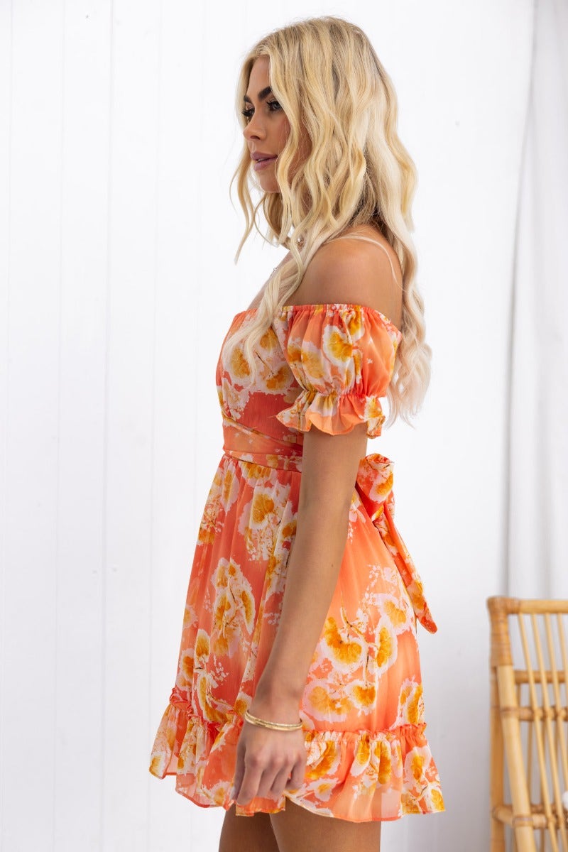 Side view of a model wearing a floral Golden Sunset Dress with off-shoulder sleeves and a fabric tie.