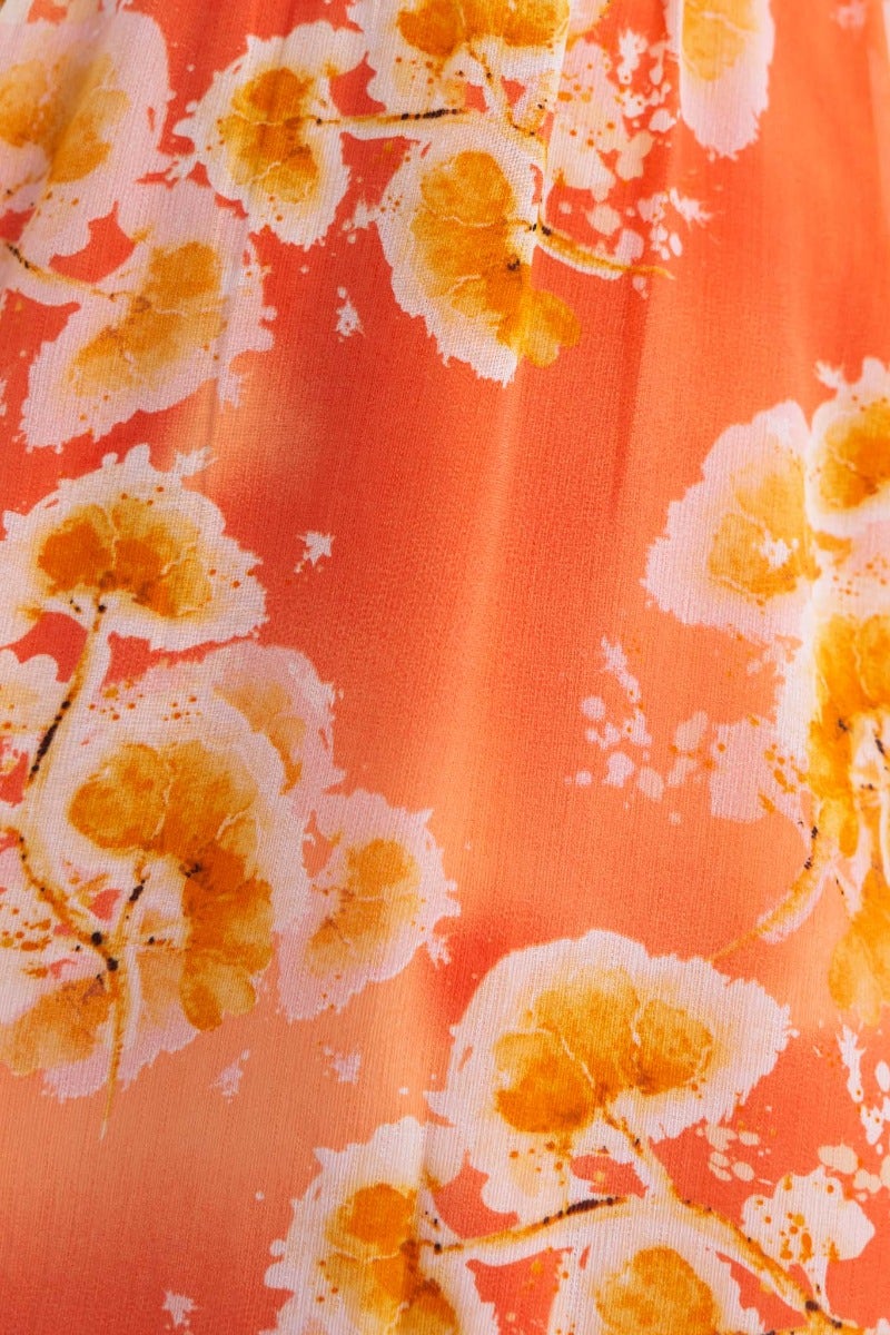 Close-up of floral print in golden hues on a vibrant sunset orange fabric, perfect for a summer dress.