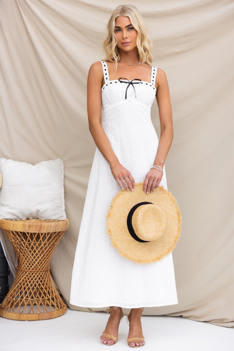 Model wearing a Cottage Dreams Maxi Dress with adjustable straps and ribbon detailing, holding a straw hat.