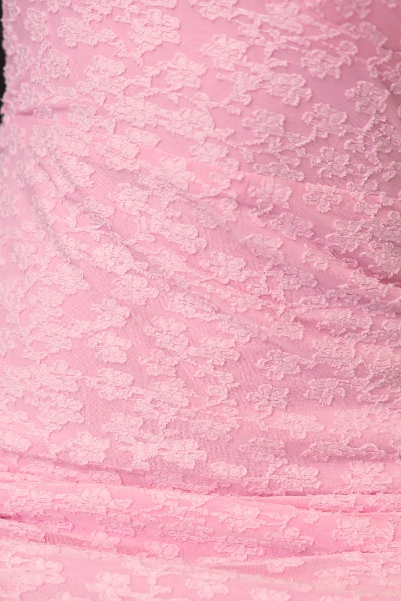 Close-up of textured pink fabric, showcasing detailed floral pattern, ideal for dresses and feminine apparel.