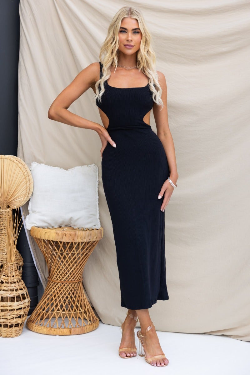 Black ribbed midi dress with square neckline and cut-out at waist, styled with strappy shoes and woven decor.