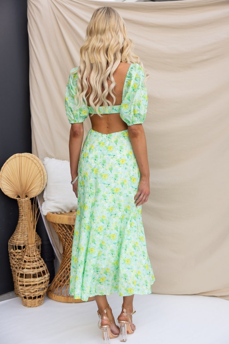Back view of a model wearing a zesty floral print midi dress with puff sleeves and cut-out waist.