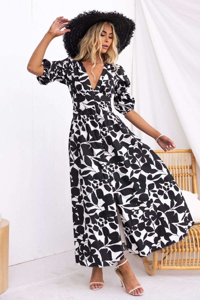 Model wearing Zohar black and white floral maxi dress with V-neckline and puff sleeves, styled with a wide-brimmed hat.