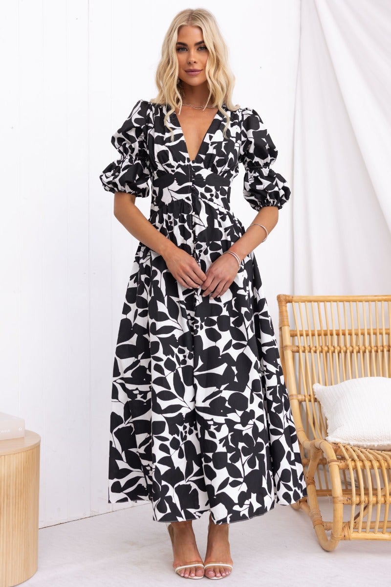 Black and white floral Zohar maxi dress with V-neckline and puff sleeves, styled with sandals in a minimalist setting.