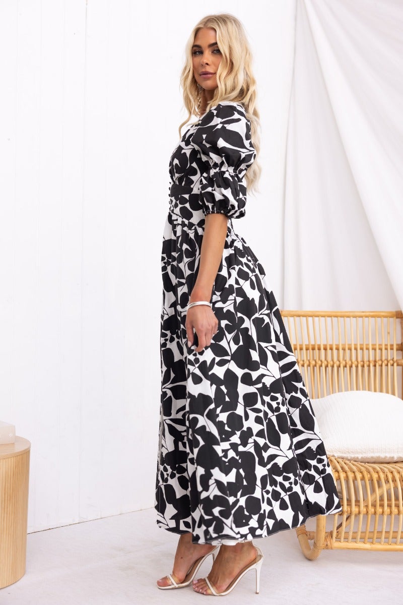 Model wearing a floral black and white maxi dress with puff sleeves and a flowing silhouette, styled for a chic look.