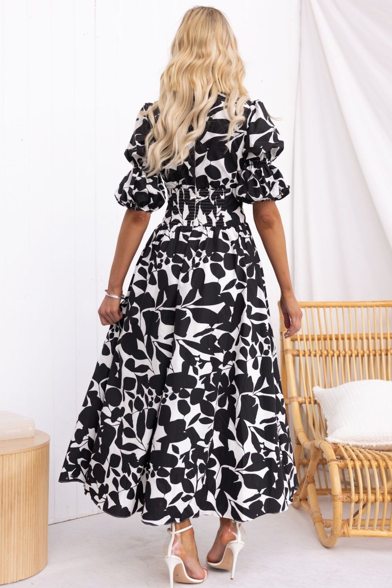 Model wearing Zohar Maxi Dress in black and white floral pattern, showcasing back design and puff sleeves.