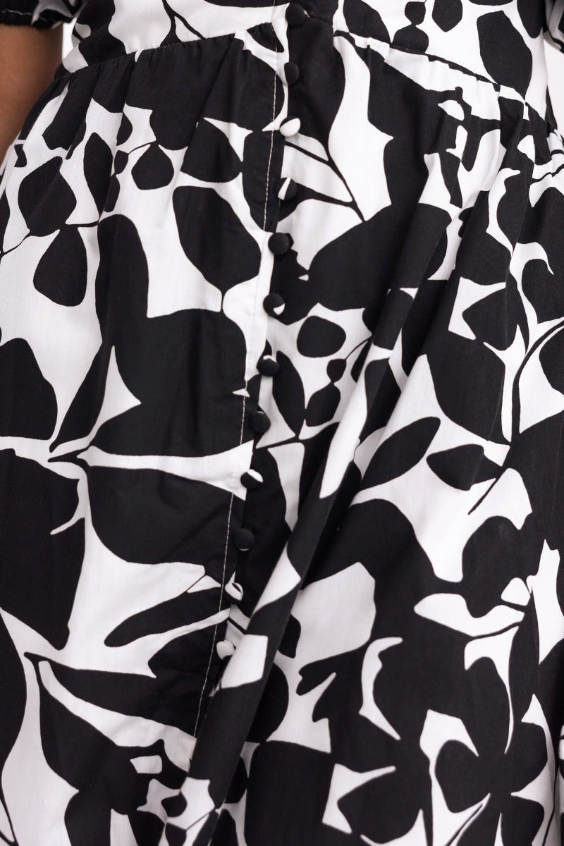 Close-up of a black and white floral patterned maxi dress showing faux button details and gathered fabric.
