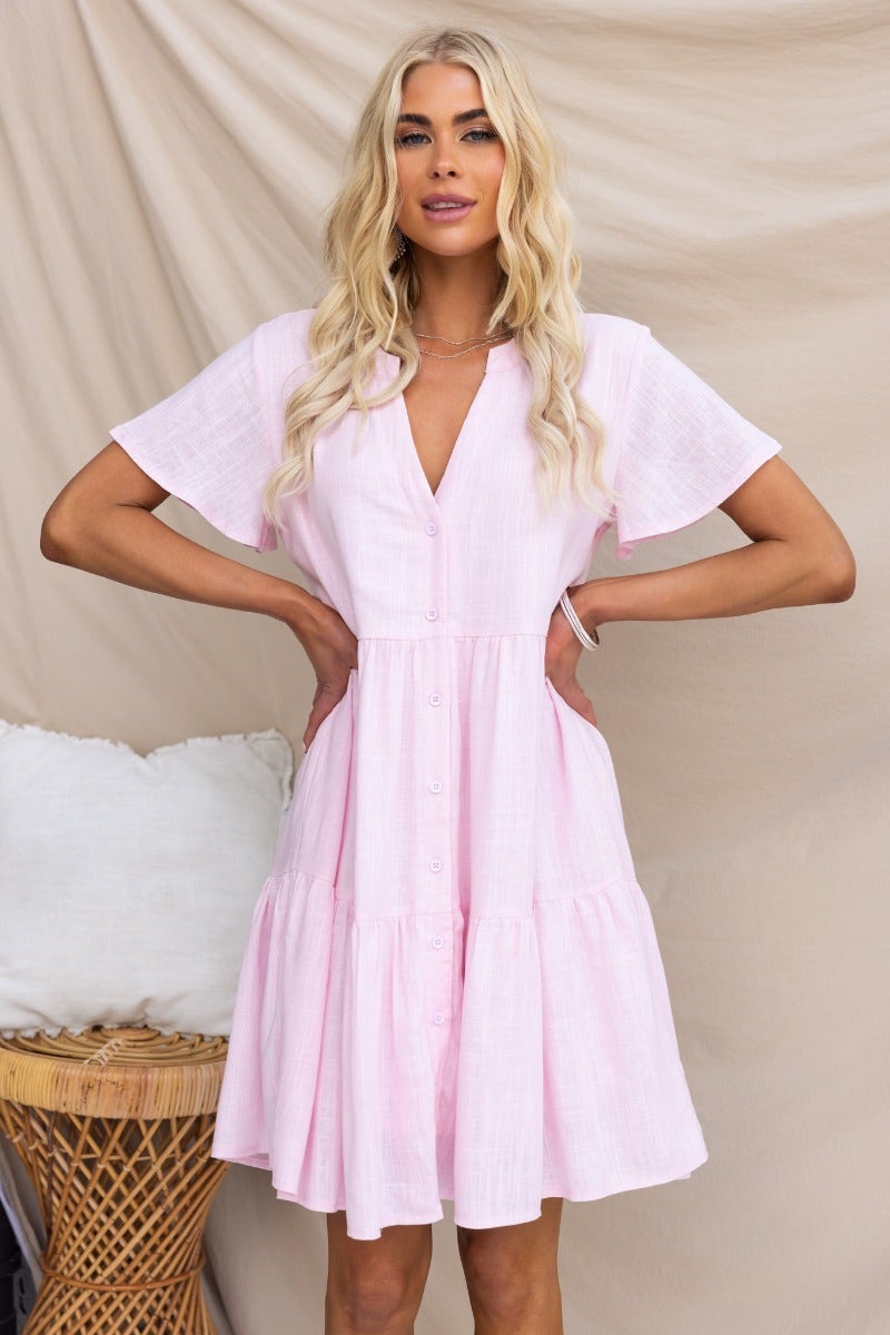 Arla Dress: Pink linen blend dress with V-neckline and button-up front, featuring a relaxed fit and short sleeves.