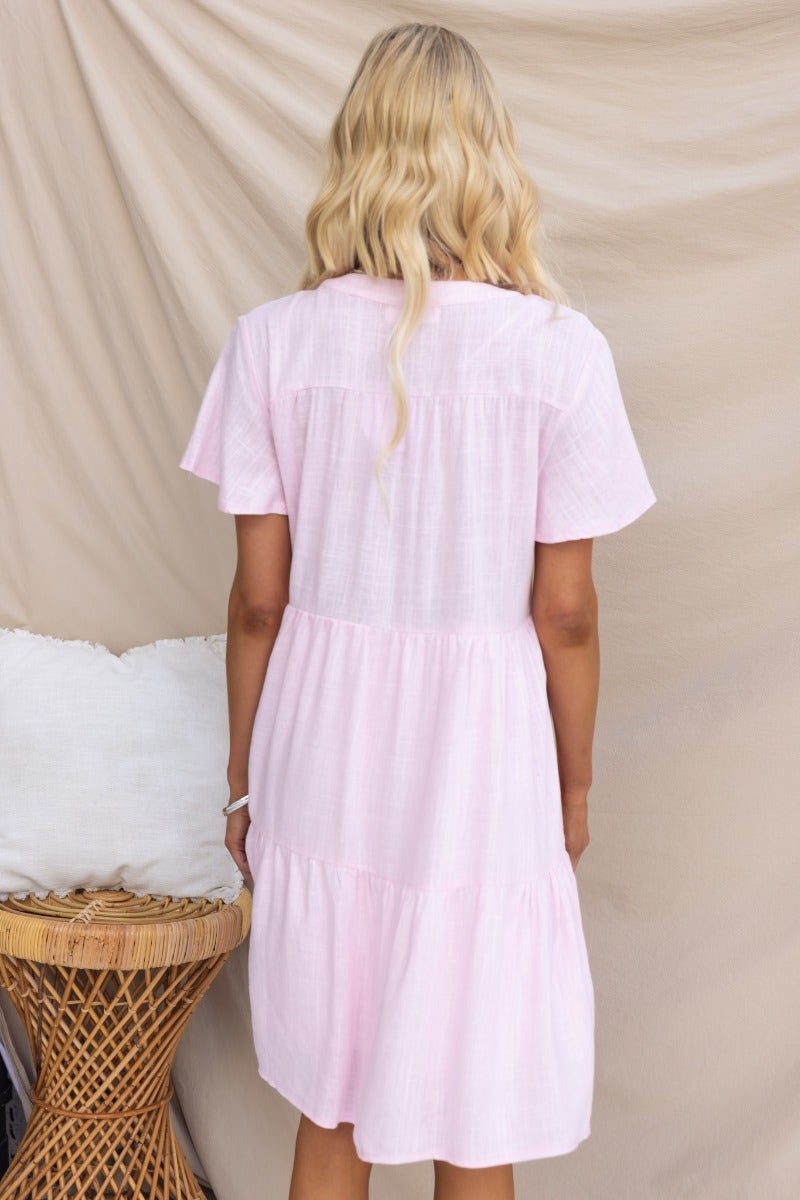 Back view of Arla Dress in light pink, featuring a V-neckline and tiered skirt design.