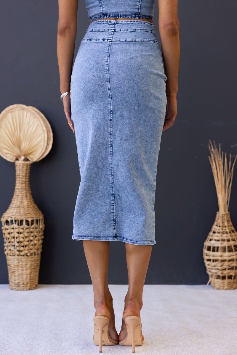 Back view of the Genevieve denim midi skirt featuring a button-up front and high split, styled with heels.