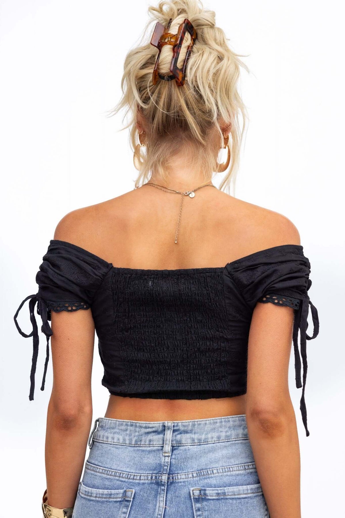 Back view of a woman in a black Hays top with ruching and ties at sleeves, styled with high-waisted jeans.