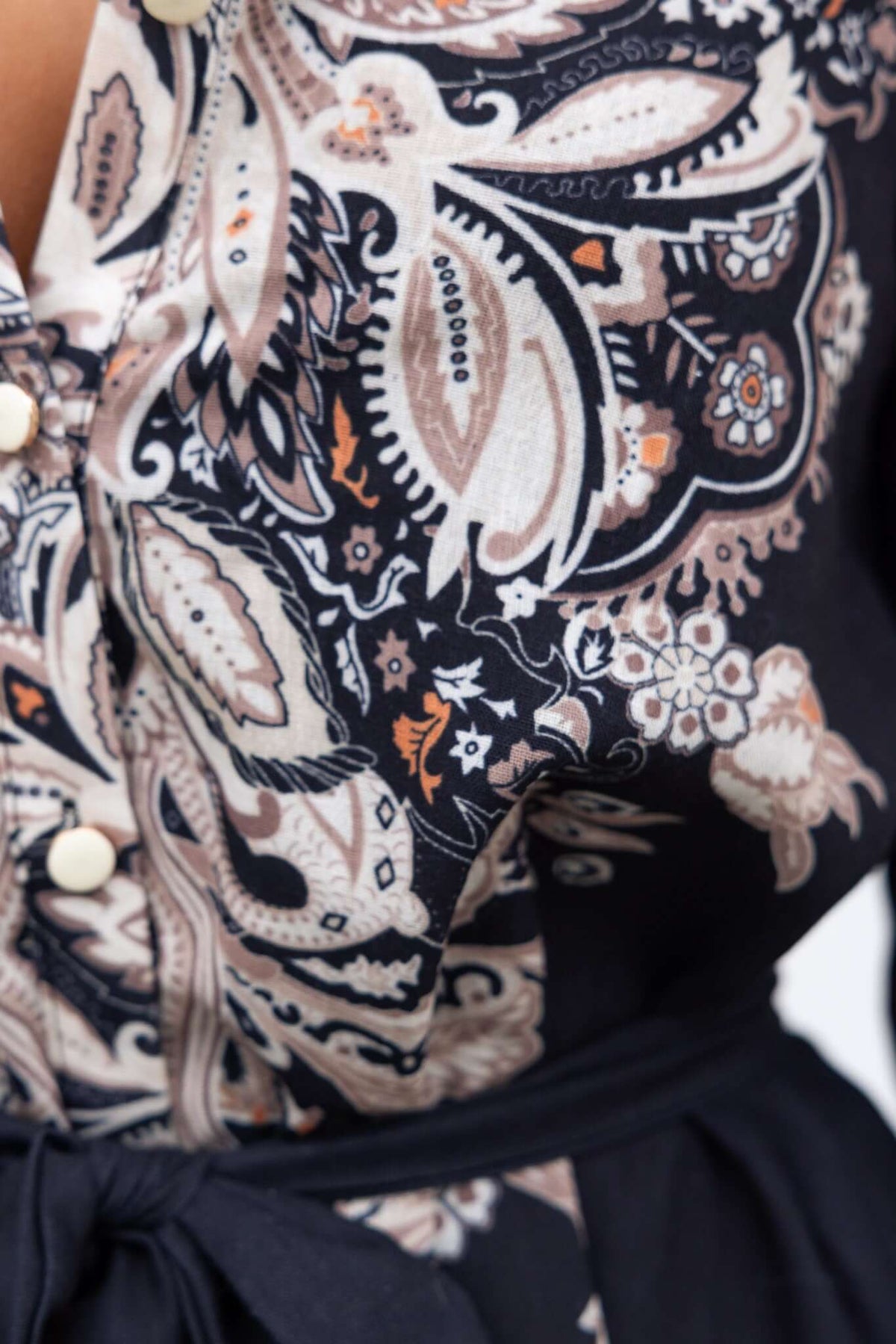 Close-up of the Channey Dress featuring a black and paisley patterned fabric with a button-up front and removable tie.