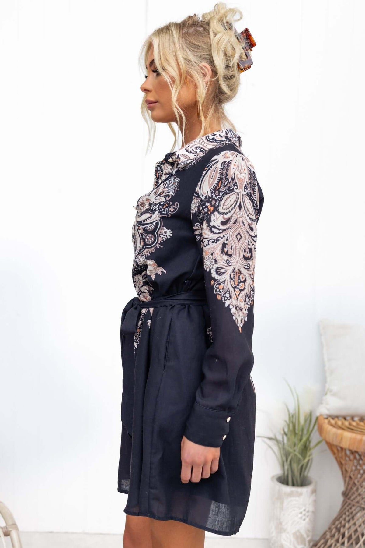 Side view of the Channey Dress in black with a paisley print, collar, button-up front, and removable tie.