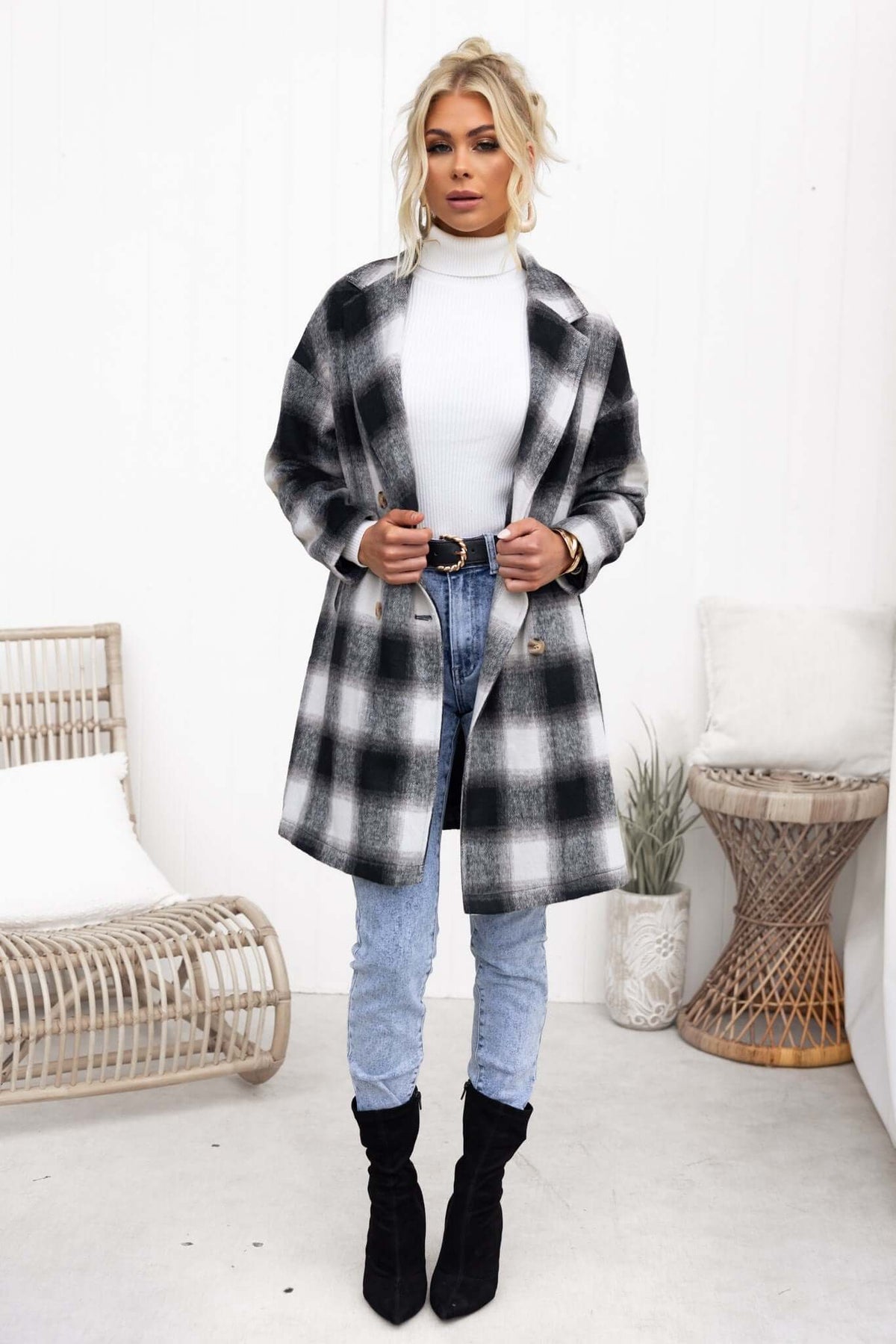 Model wearing a black and white plaid Tiffin coat over a turtleneck, styled with jeans and boots, in a light interior setting.