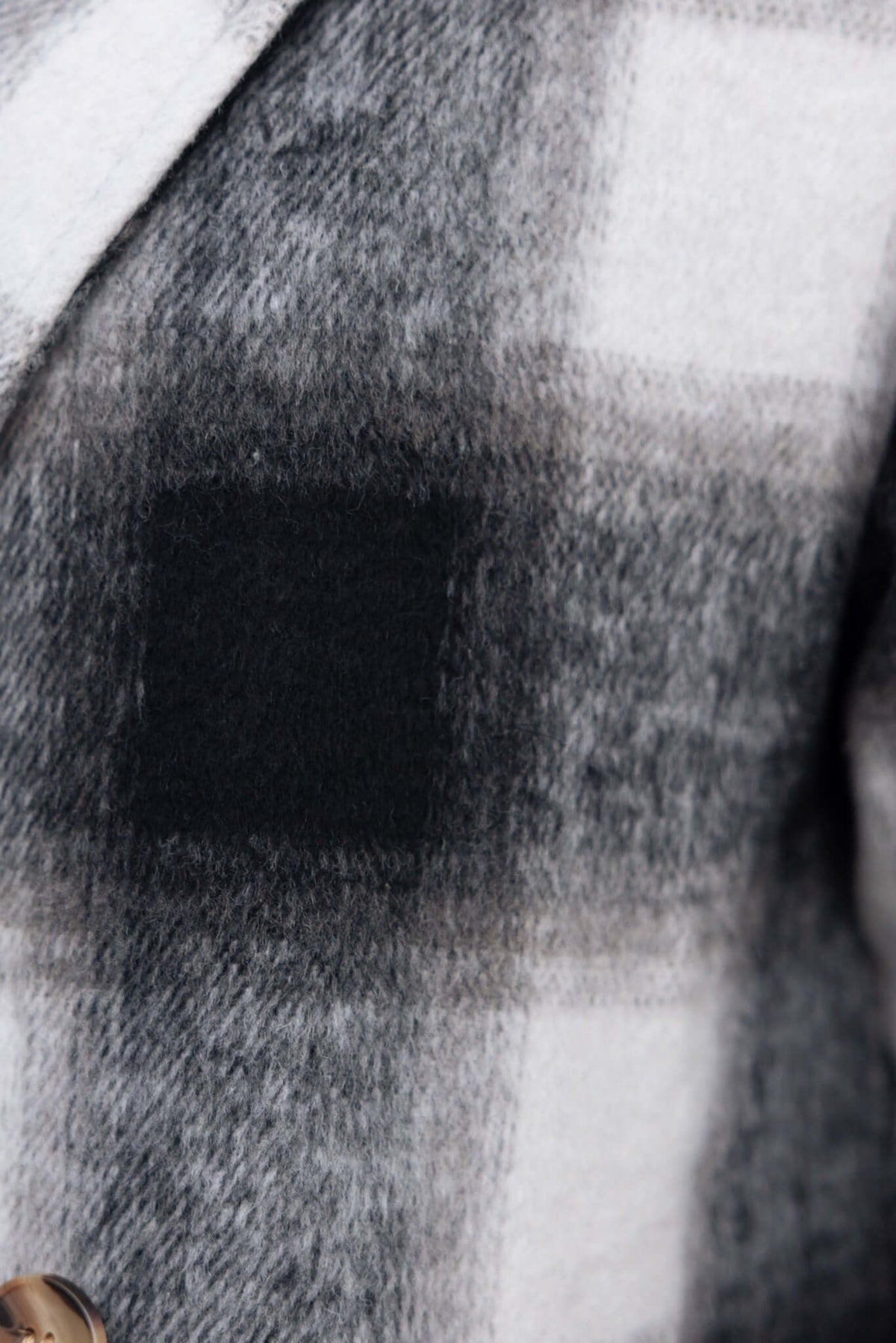 Close-up of a black and white plaid fabric on a Tiffin coat, featuring a stylish texture and button detail.