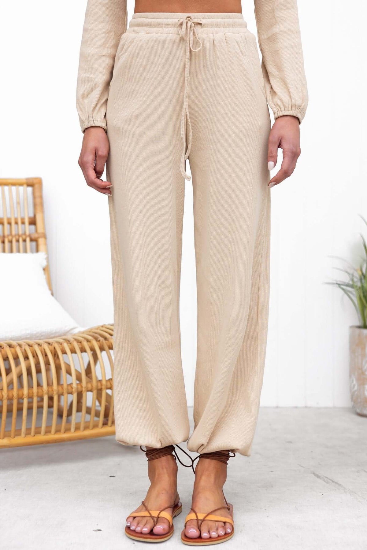 Beige Micah Pants with elastic waistband, pockets, and drawstring, paired with sandals, in a stylish setting.