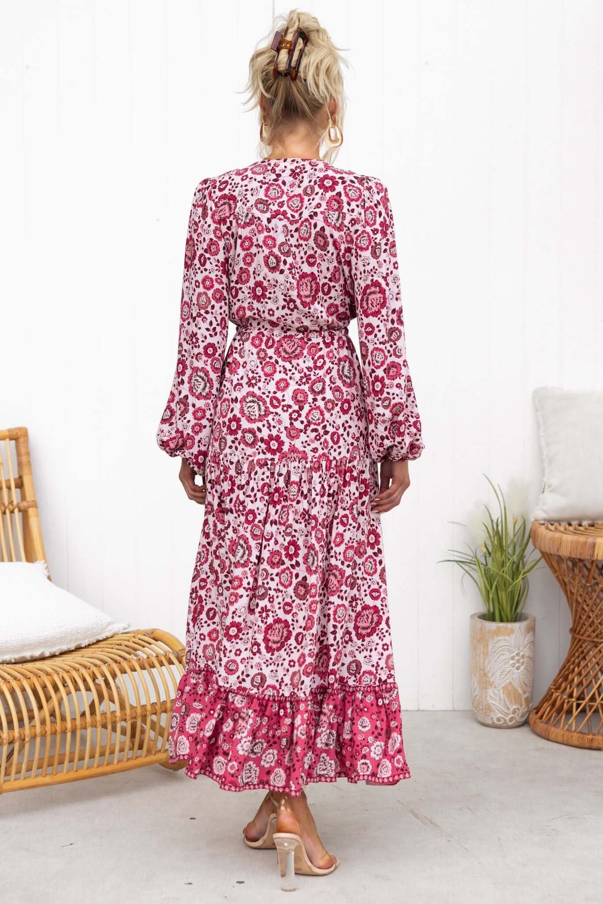 Back view of a woman in a floral pink Sarzana Maxi Dress, featuring elastic sleeves and a drawstring waist.