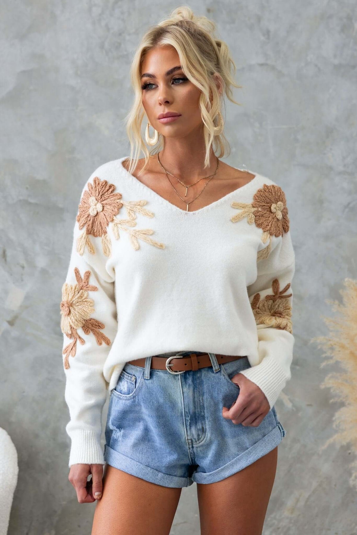 Capa Jumper with V-neckline and embroidered flowers, styled with denim shorts and layered necklaces.