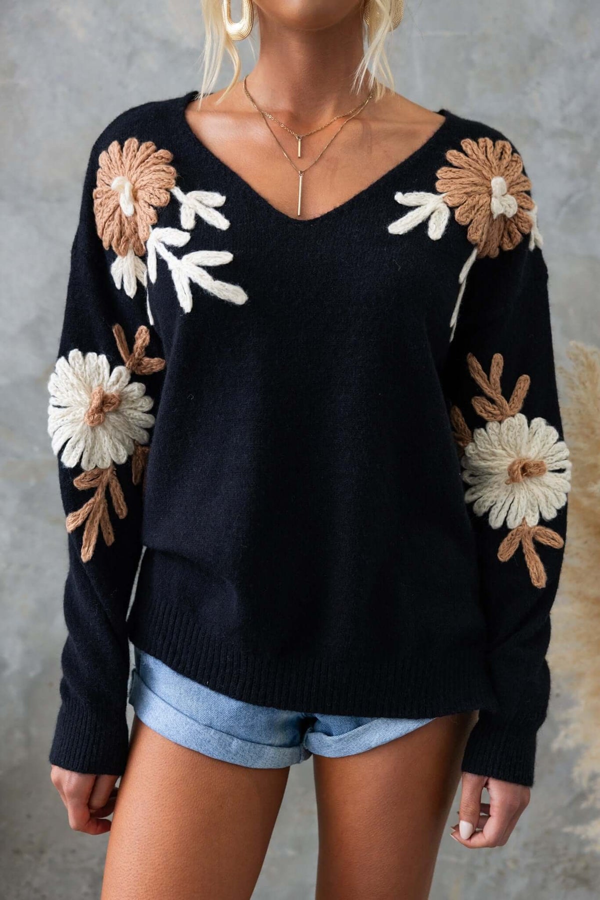 Black Capa Jumper with floral embroidery and V-neckline, styled with shorts and an elegant necklace.