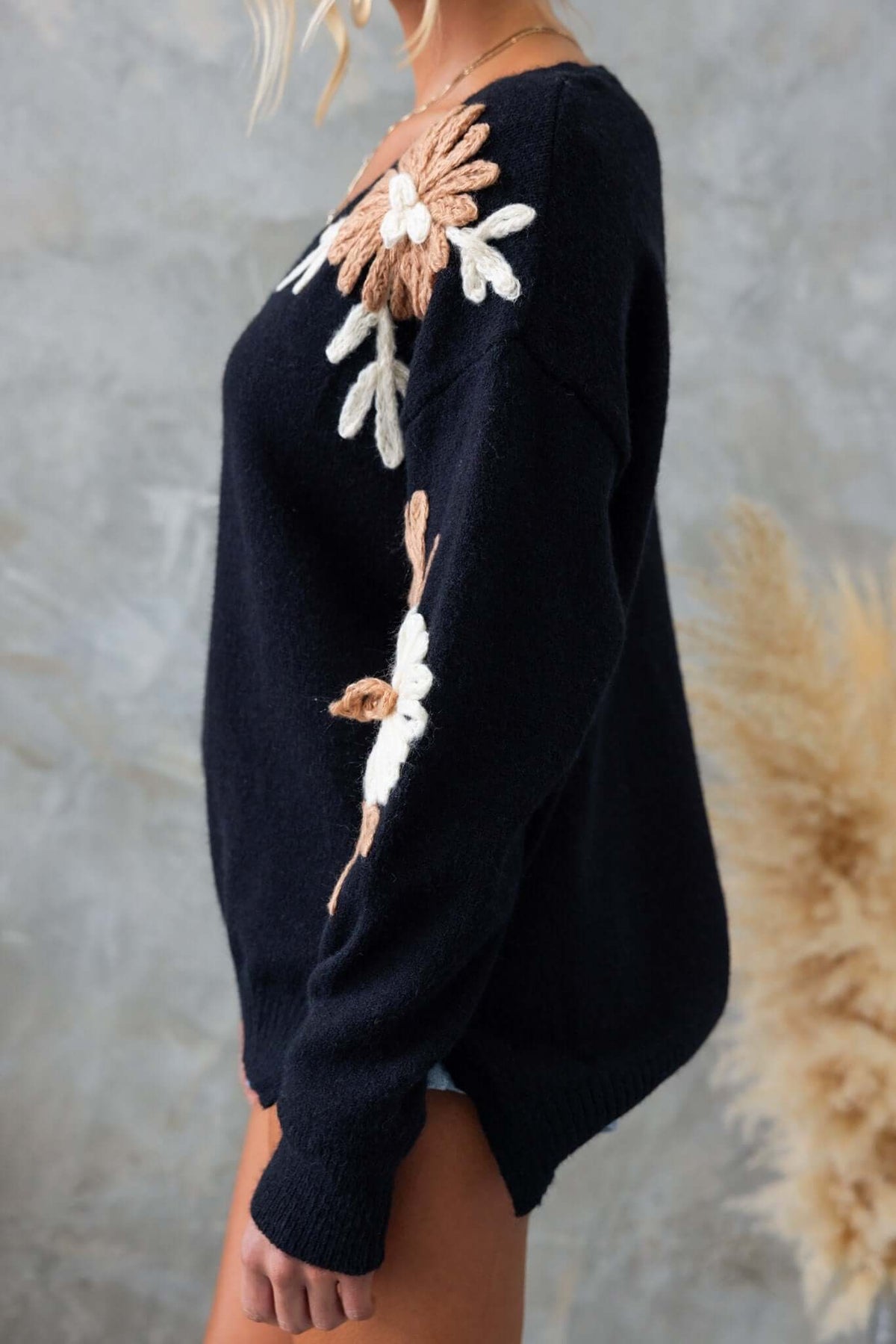 Black jumper with floral embroidery, V-neckline, and side splits, showcasing a relaxed fit and textured knit material.