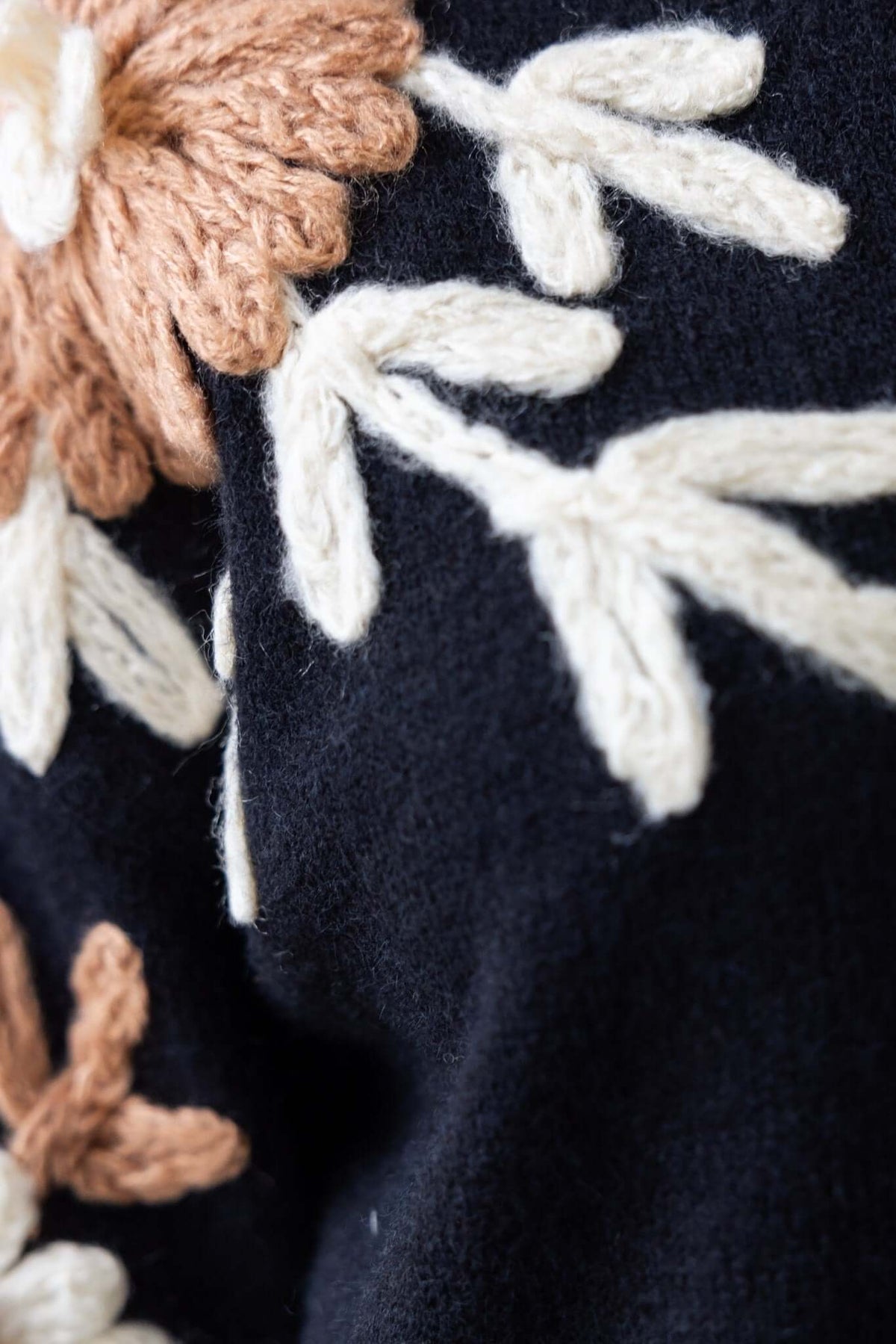 Close-up of black jumper with colorful floral embroidery in cream and tan hues, showcasing intricate knit design.