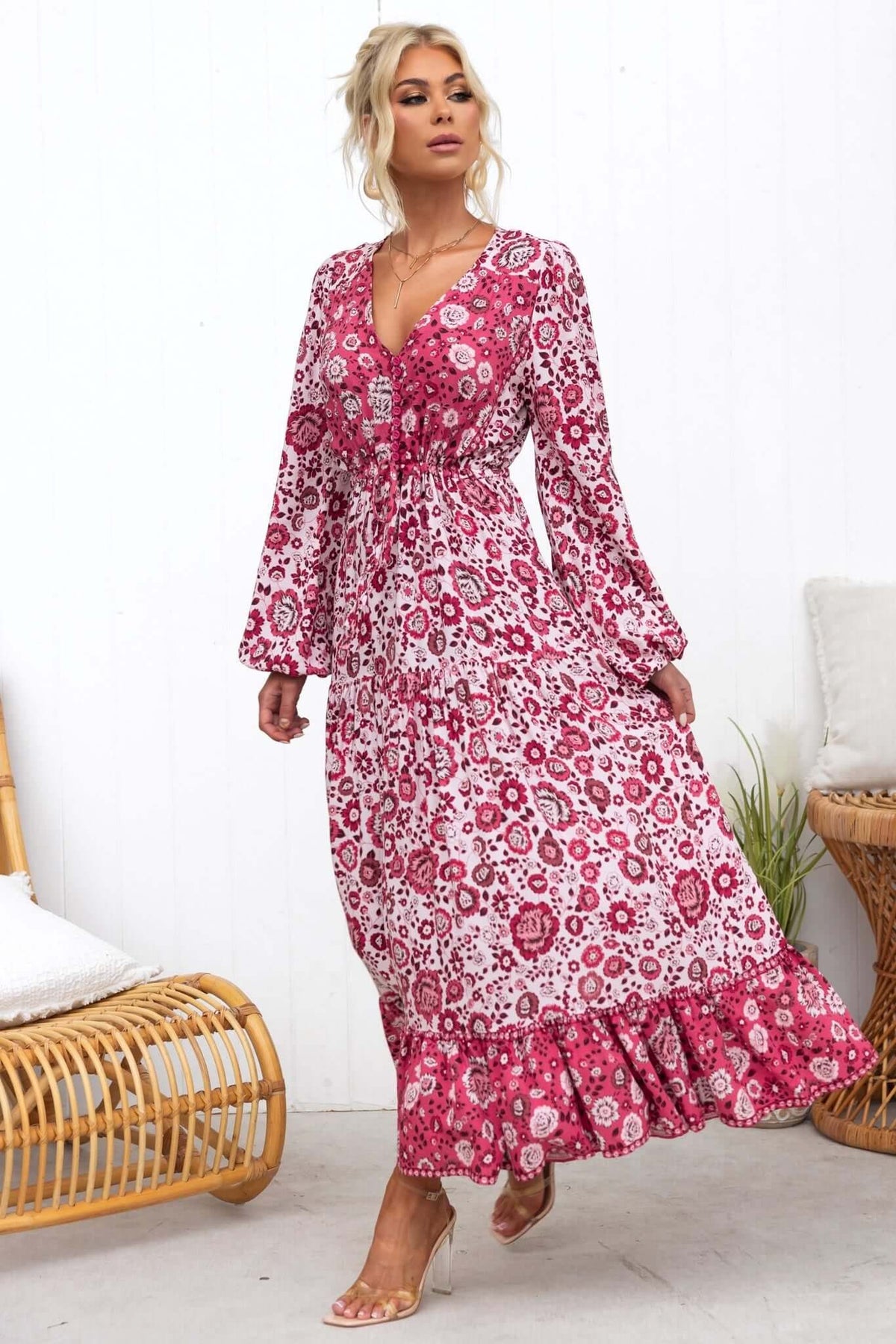 Sarzana Maxi Dress in pink floral print, featuring button-up bust and elastic sleeves, styled on model in a cozy setting.
