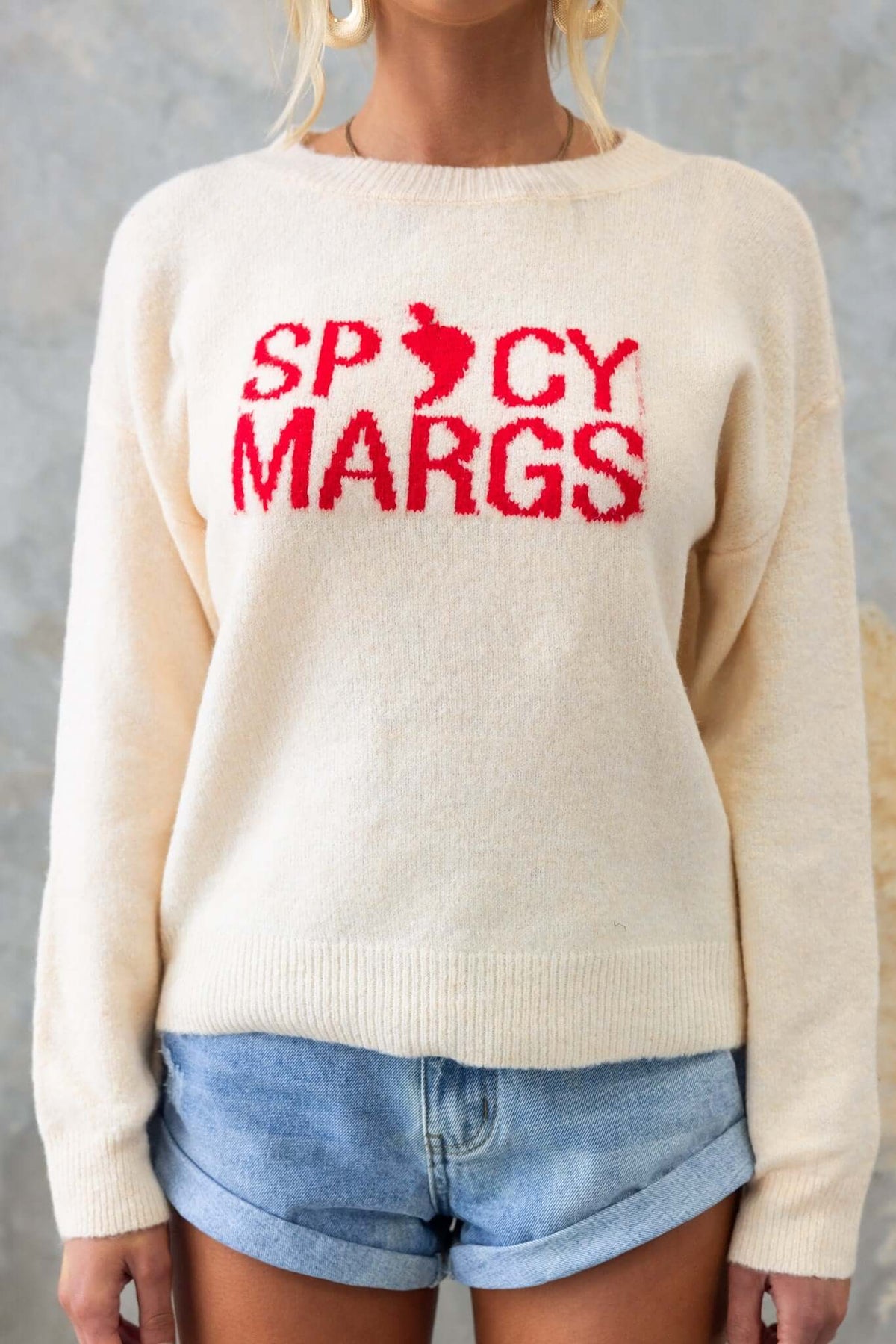 Tommy Jumper in cream color with red 'Spicy Margs' print, worn with denim shorts, showcasing a relaxed fit.