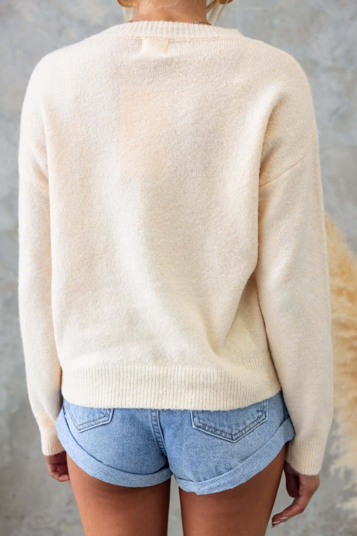 Back view of a creamy Tommy jumper styled with denim shorts, showcasing its knit texture and relaxed fit.