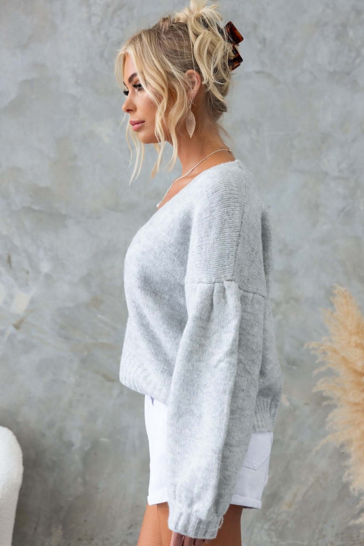 Side view of a woman wearing a gray Irvine Cardigan with a relaxed fit and V-neckline, styled with denim shorts.