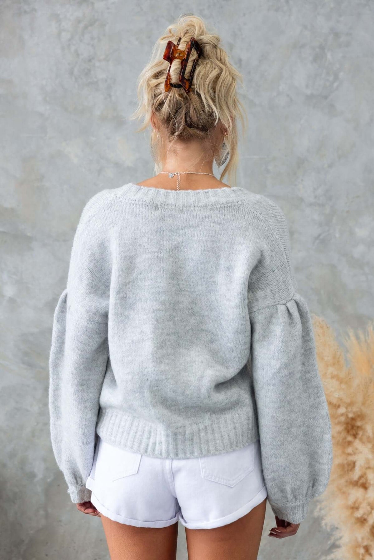 Back view of a woman in a cozy gray cardigan, complemented by a stylish hair clip and casual white shorts.