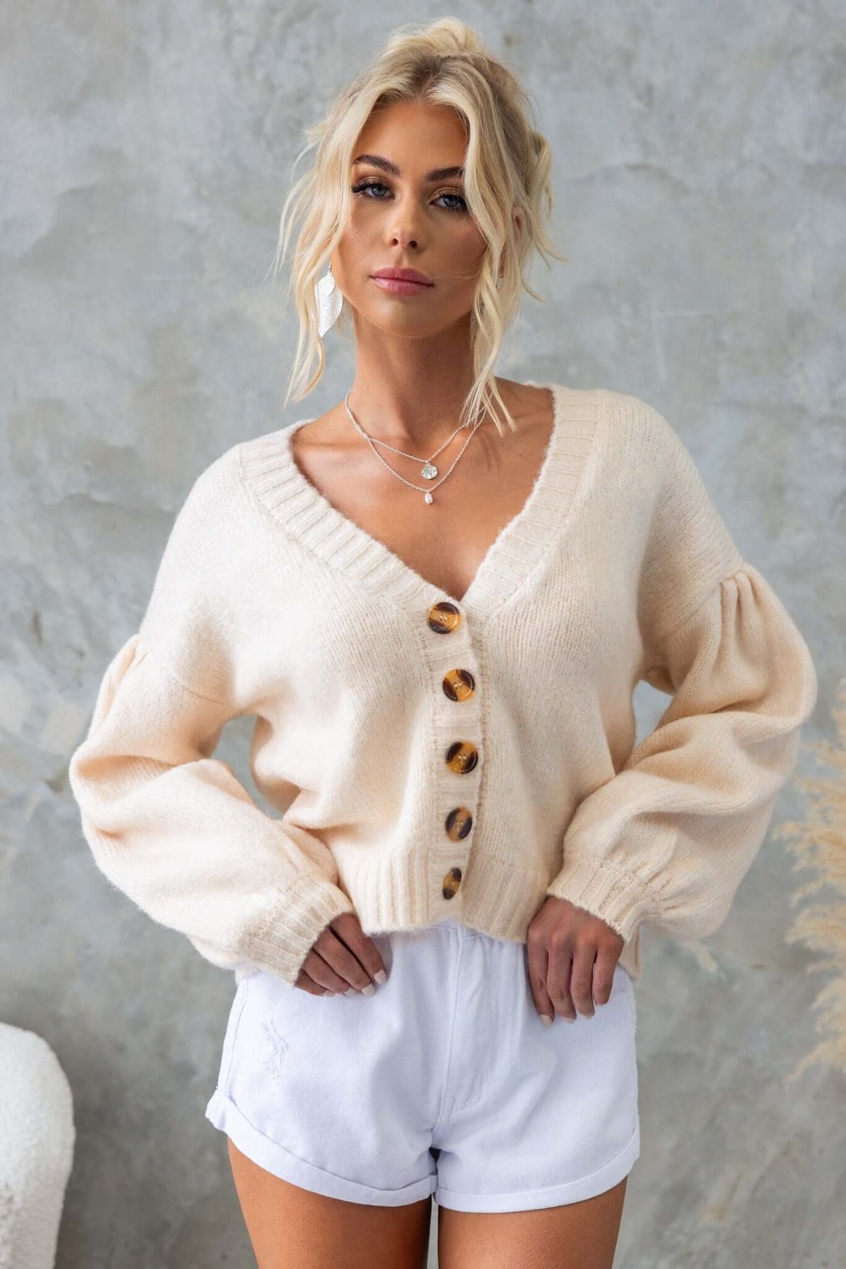 Model wearing an Irvine Cardigan with a V-neckline and button-up front, paired with white shorts.