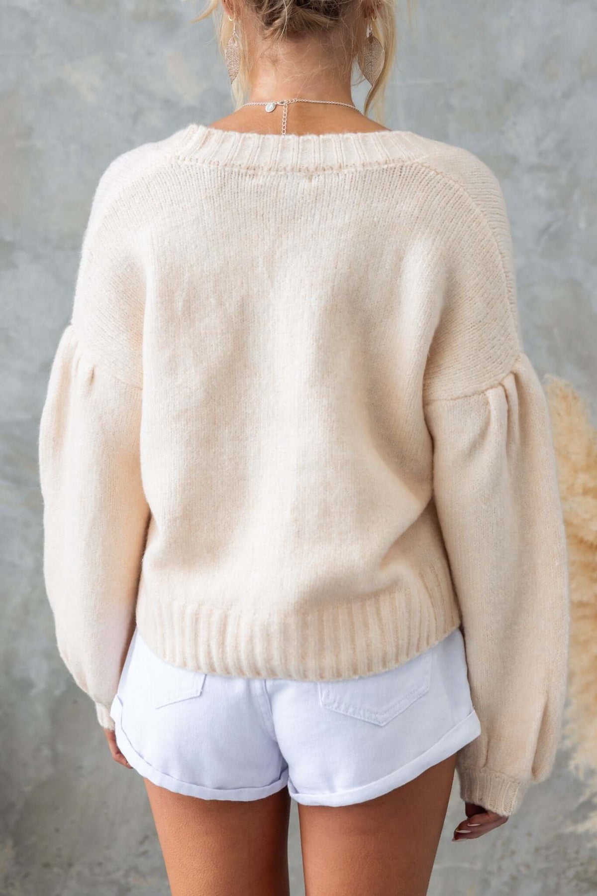 Back view of a model wearing a cream-colored Irvine Cardigan with puffed sleeves and relaxed fit.