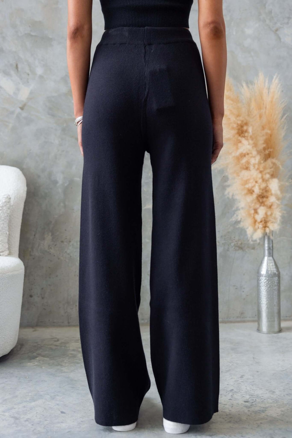 Back view of Nowlan Pants, black mid-high waist with drop crotch style, featuring an elastic waistband and ribbed knit material.