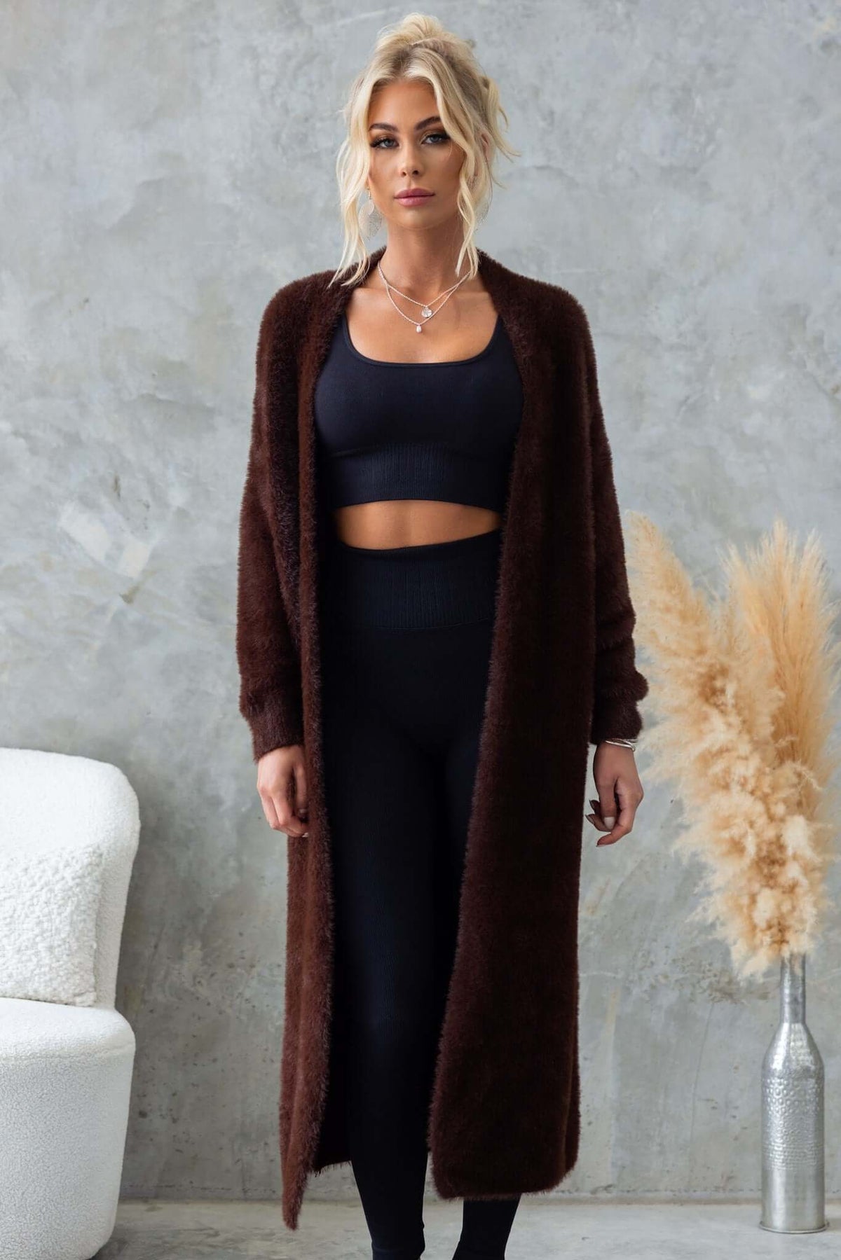 Model wearing the Salem Cardigan in brown, featuring a longline fluffy knit design, styled with a black crop top and leggings.