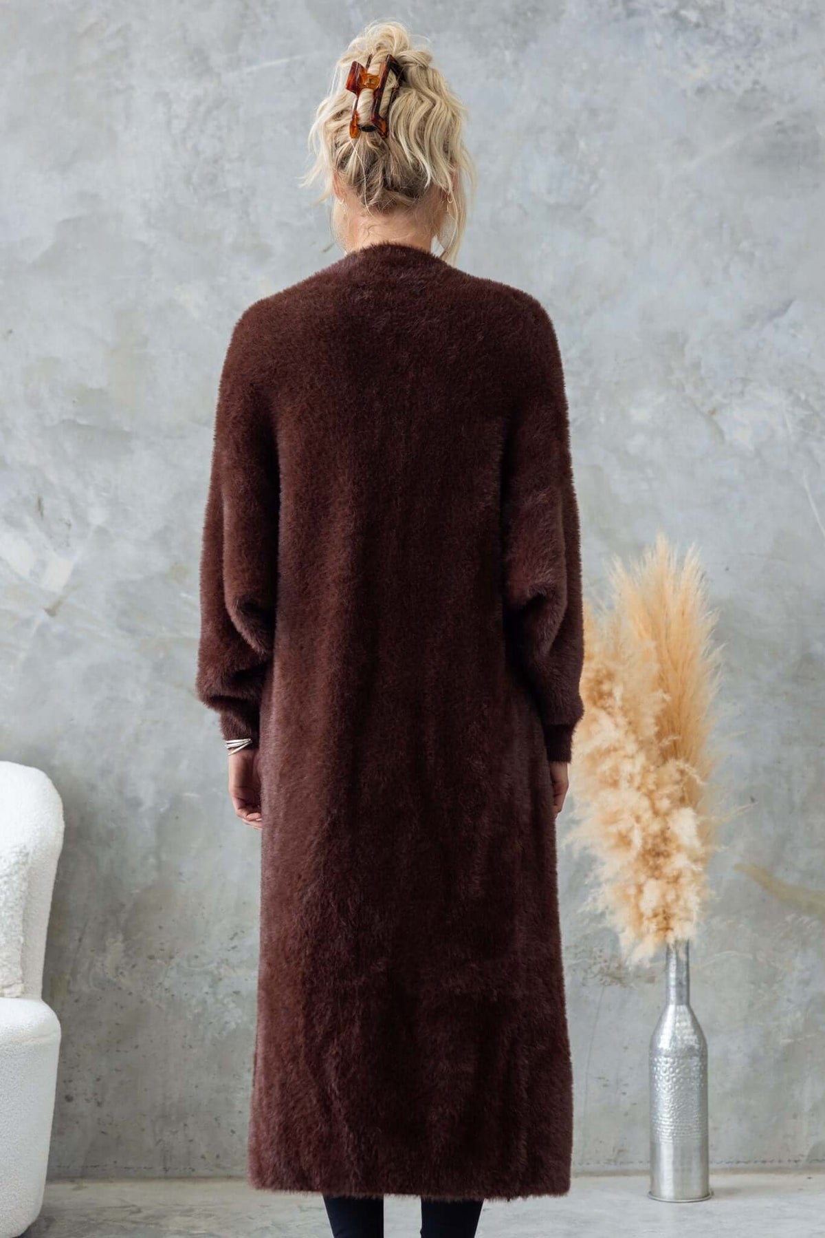 Back view of a woman in a long brown fluffy cardigan styled with a ponytail in a cozy setting.