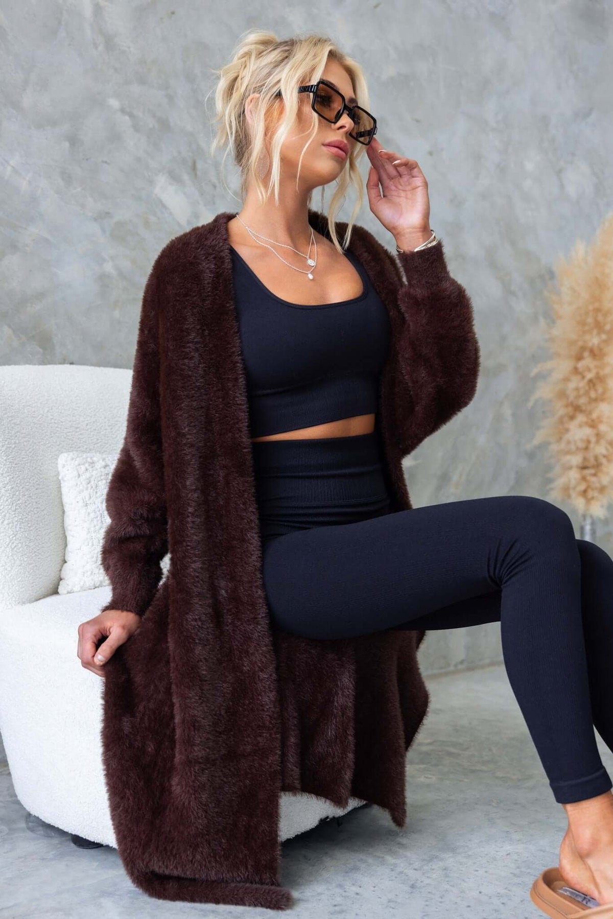 Model wearing a brown fluffy Salem Cardigan over a black outfit, sitting on a chair with a relaxed pose.