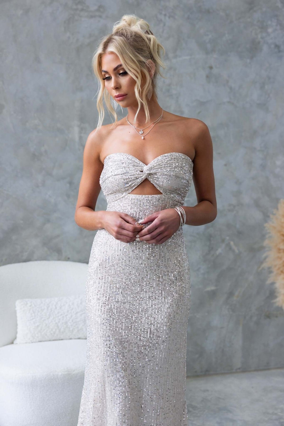 Model wearing Kileen Maxi Dress, a strapless sequin gown with cut-out at bust and elastic back, against a textured wall.