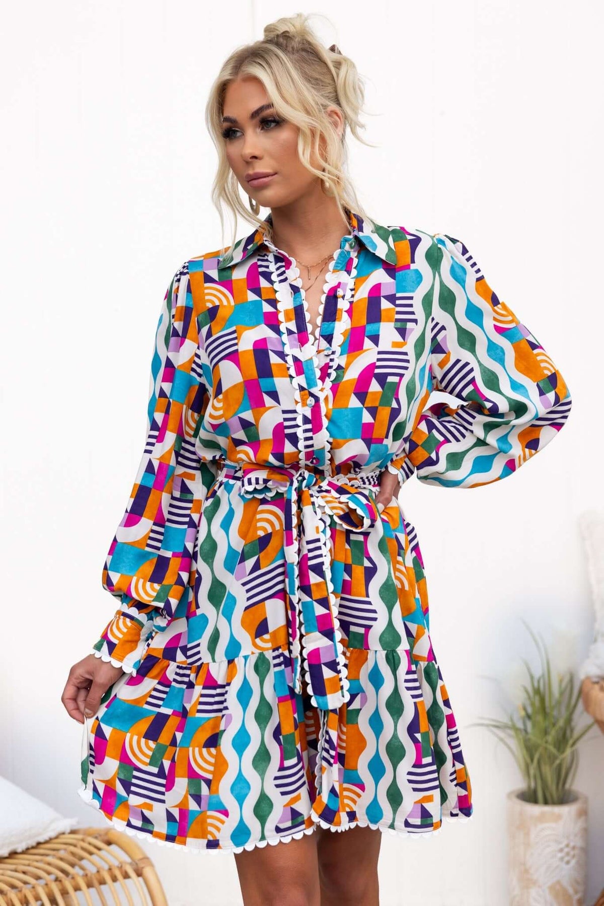 Model wearing the Bransley Dress, featuring a colorful pattern, button-up front, and removable tie.