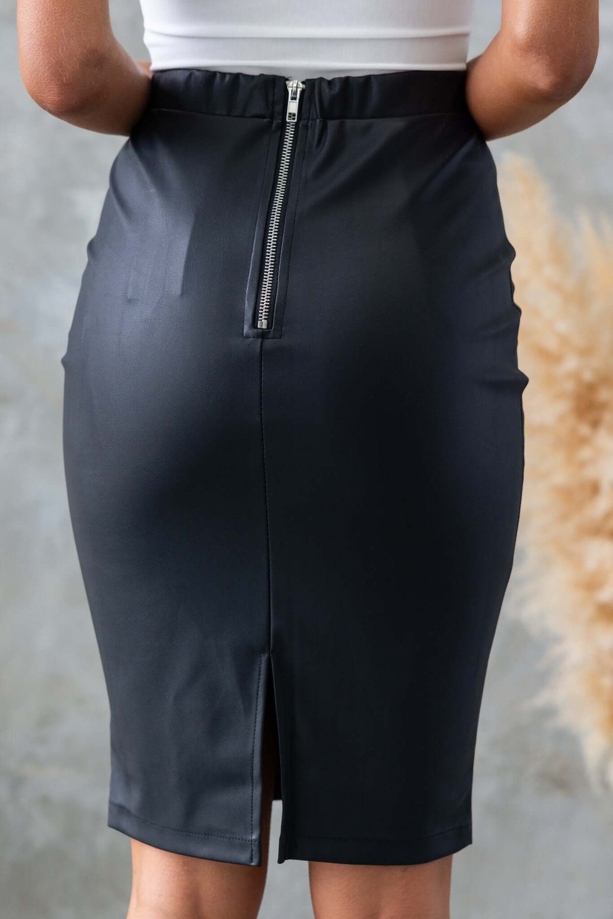 Back view of the Udine Midi Skirt featuring a zip closure, elastic waistband, and back split in faux leather.