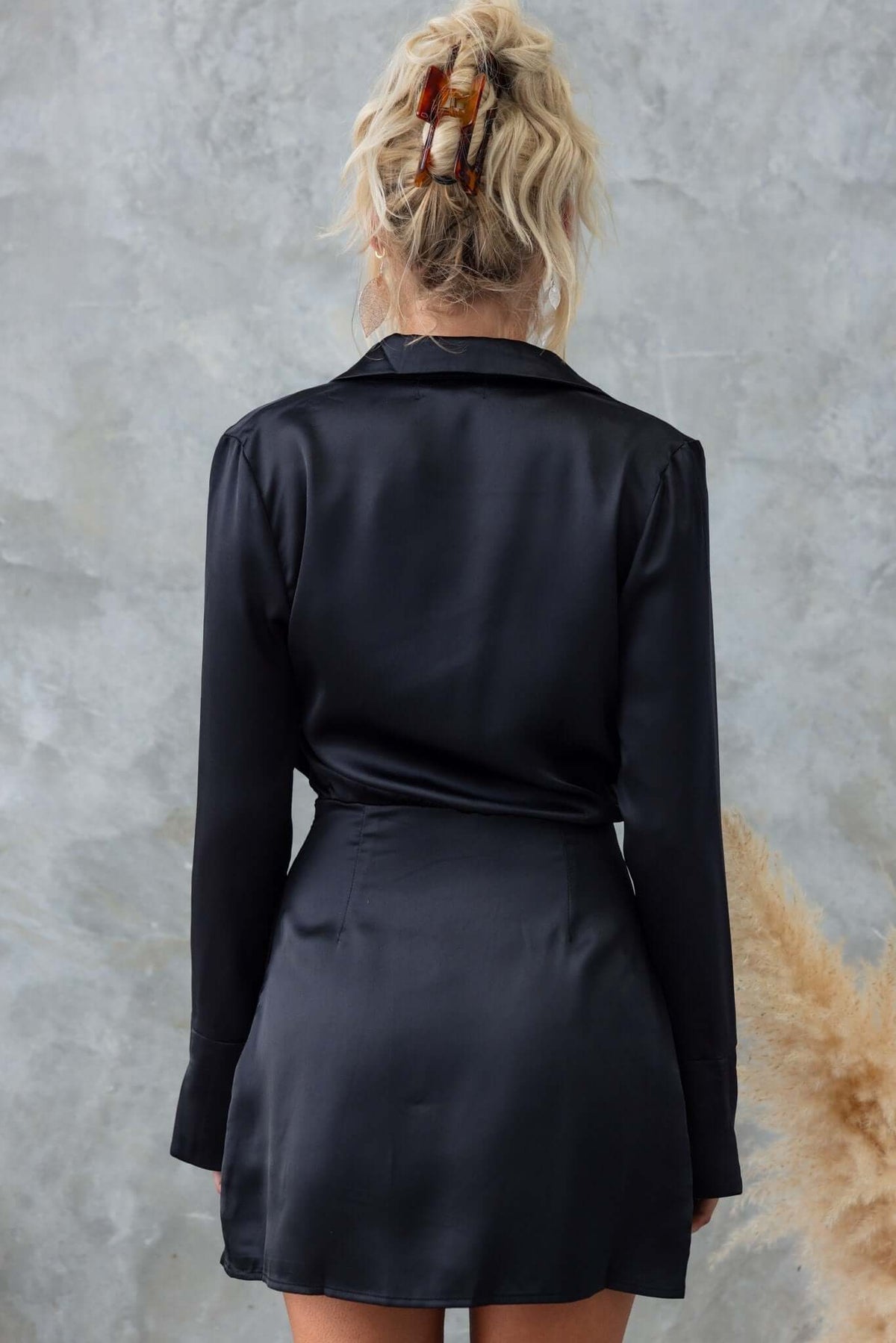 Back view of the Vallejo Dress, a black satin dress with a collar and long sleeves, showcasing its asymmetric hemline.