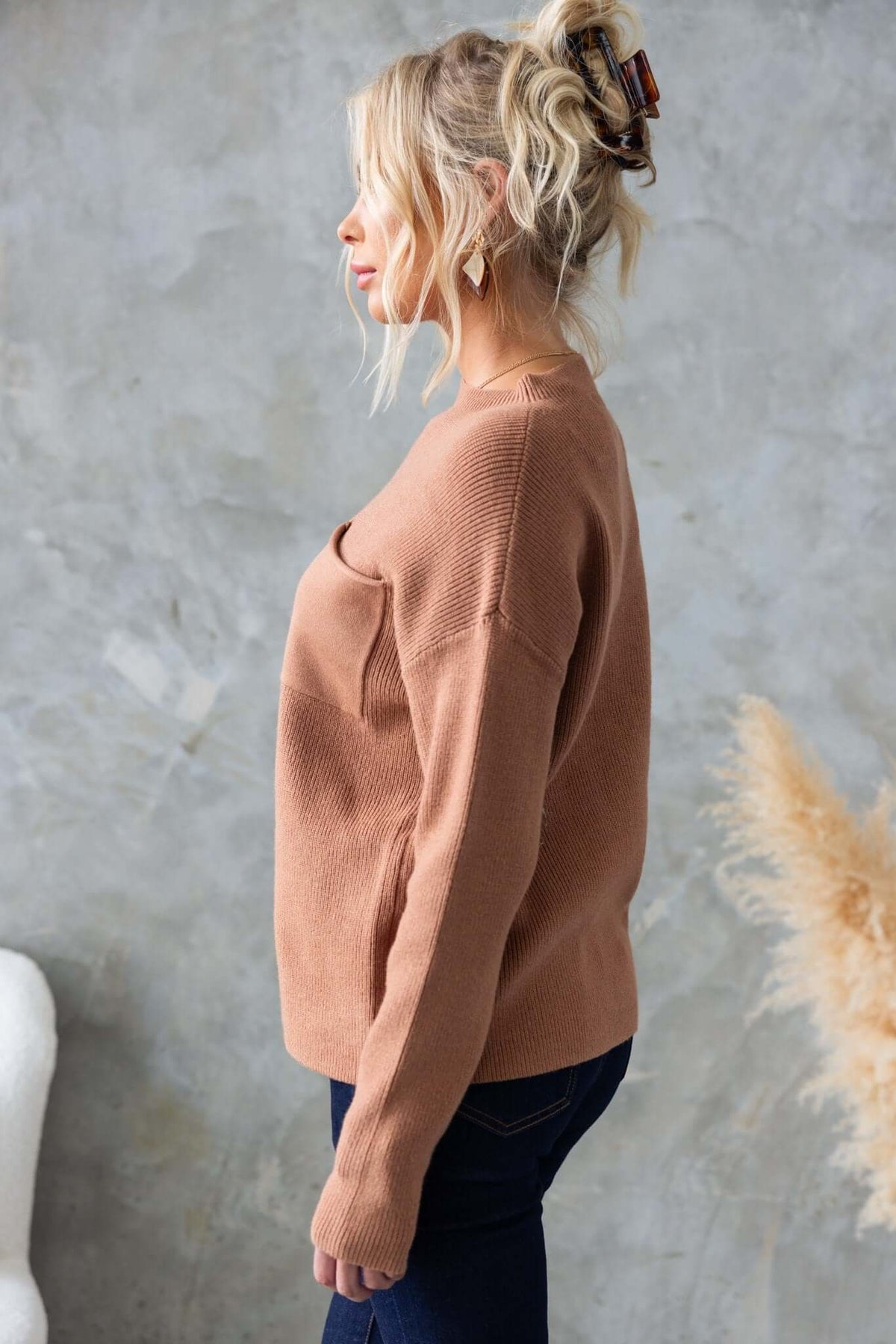 Side view of a woman wearing a tan Palladia Jumper, showcasing its round neckline and ribbed knit texture.