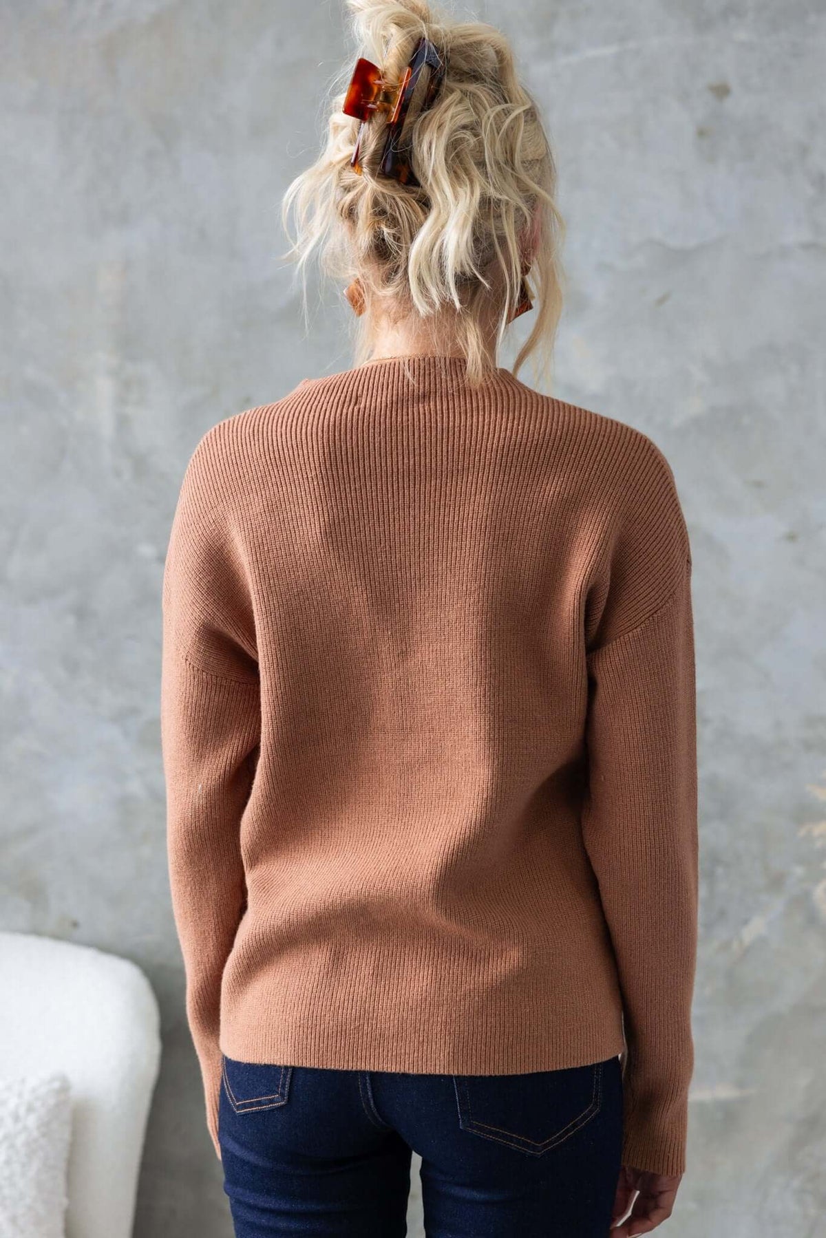 Back view of a woman wearing a brown ribbed knit Palladia Jumper with a relaxed fit, styled with denim jeans.