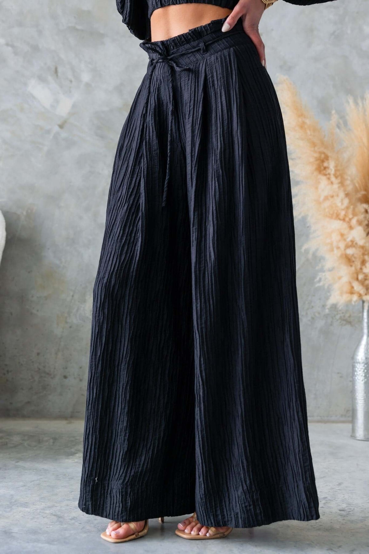 Mid-high waist black textured pants with removable tie and pockets, styled for a chic and relaxed look.