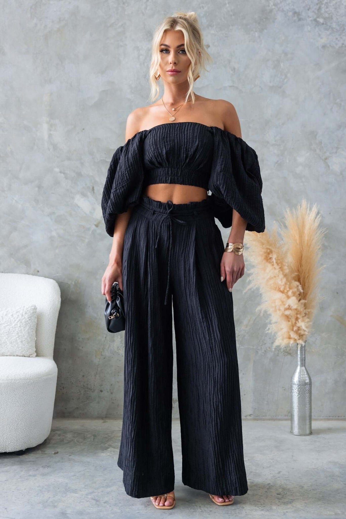 Model wearing a textured black off-shoulder top with wide-legged pants, showcasing stylish design and a modern look.