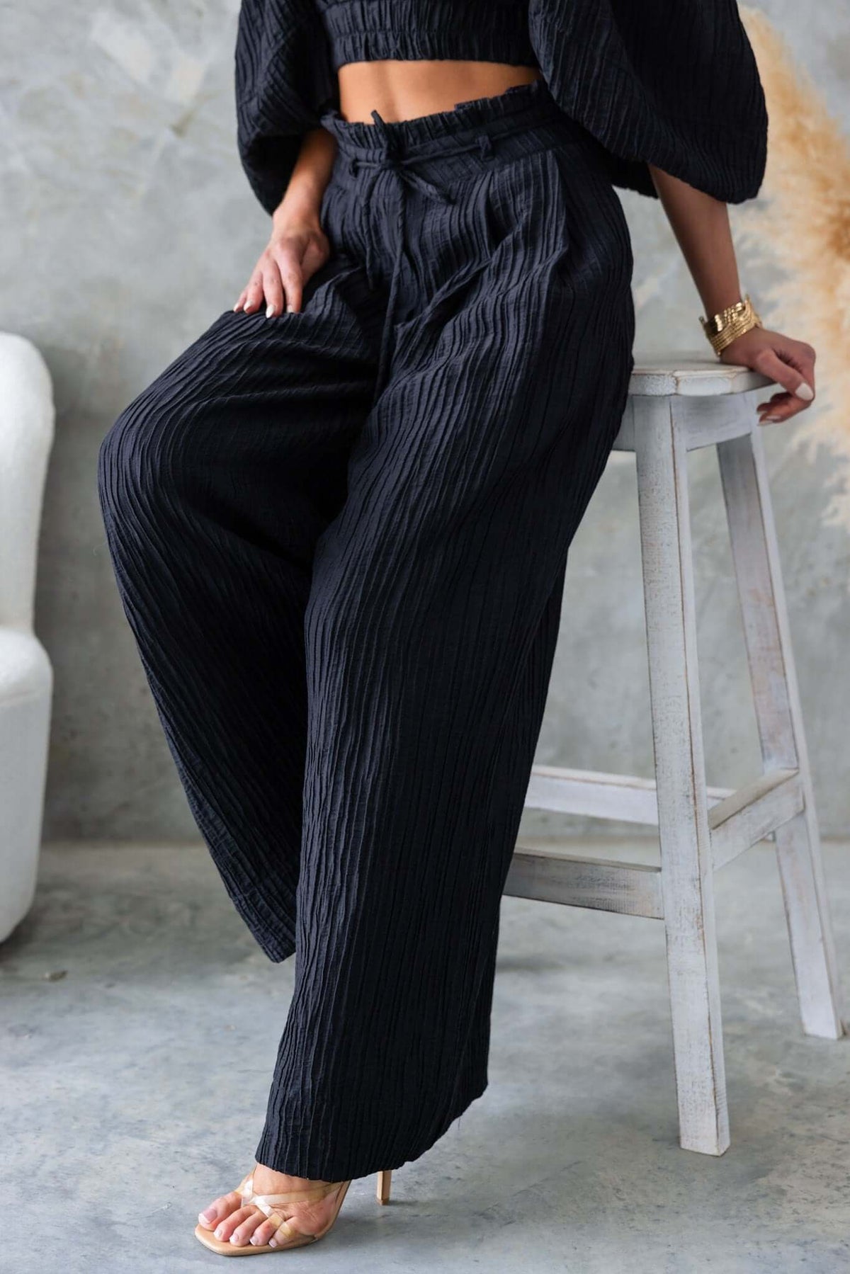 Black textured mid-high waist pants with pockets and removable tie, styled with a matching top.