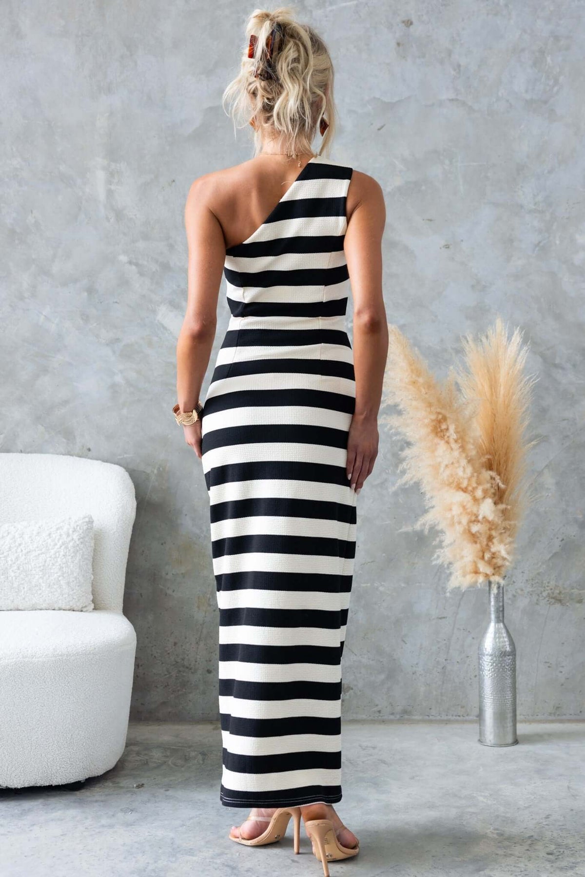 Woman in a Caserta Maxi Dress featuring a one-shoulder design and bold black and white stripes, styled in a chic setting.